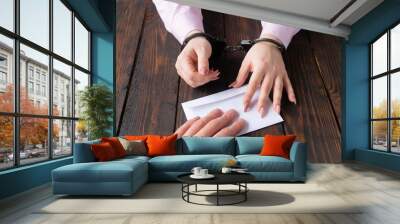 men's hands give money in envelope to women's hands in handcuffs against the background of a wooden table Wall mural