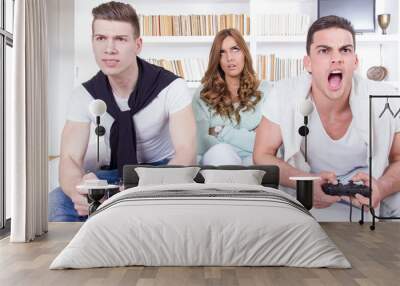 bored women between two casual passionate men playing video game Wall mural