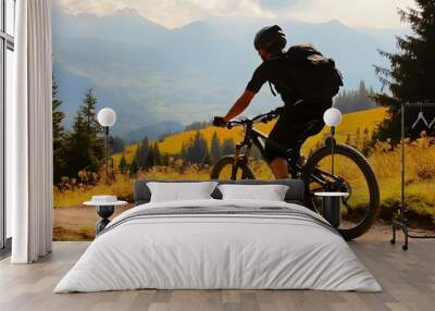 A man mountain biking on a dirt road with a beautiful mountain backdrop. Wall mural