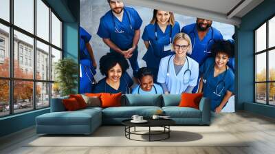 Diverse group of healthcare professionals in blue scrubs smiling and standing together, showcasing teamwork and unity in a medical setting. Wall mural