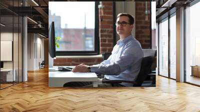 Man in blue shirt sits at desk in office Wall mural