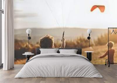 Two young boys flying kites in a sunlit open field during sunset. Wall mural