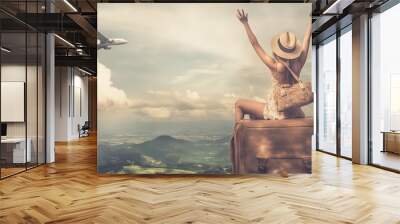 Woman celebrating travel with arms raised as plane flies by. Wall mural