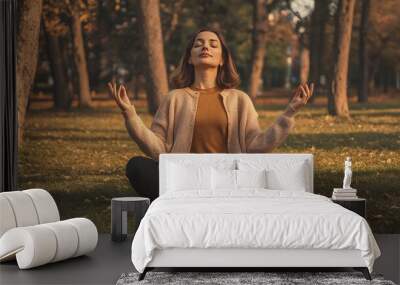 Young woman meditating in a serene autumn park, finding peace and tranquility. Wall mural