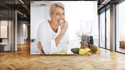 Portrait, fruit salad and apple with an elderly woman in the kitchen of her home for health, diet or nutrition. Smile, food and cooking with a happy senior female pensioner eating healthy in a house Wall mural