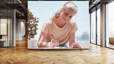 Writing, book and a senior woman author sitting outdoor in summer for inspiration as a writer. Idea, planning and notebook with a female journalist using a pen to write in a journal or diary outside Wall mural