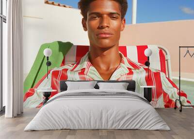 Black male model in a red and green striped shirt lounging by the pool. Summer fashion portrait with bright, sunny vibes and a casual, stylish look. Wall mural