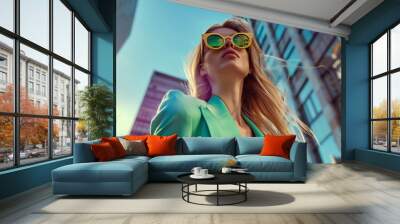 Woman model wearing a green suits and yellow sunglasses posing on the street in a low angle shot. Fashion shooting Wall mural