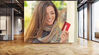 Cheerful excited young woman with credit card standing outdoors Wall mural