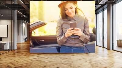 Successful woman standing by her car texting on mobile phone Wall mural