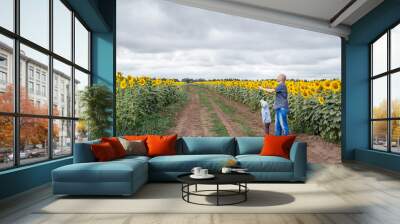 A father and son fly a kite in a field of sunflowers. Wall mural