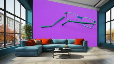 Green glasses with a broken temple against a purple background. Wall mural