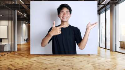 young asian man smiling gesturing right hand pointing left palm Wall mural