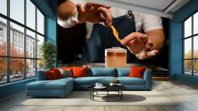 Bartender adding orange zest to a brown cocktail in the glass Wall mural