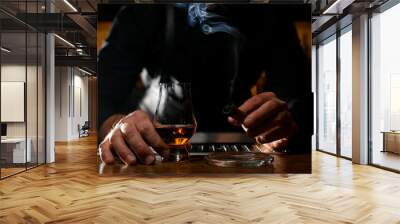 charming view on male hand holding glass with cognac and smoking cuban cigar over ashtray Wall mural