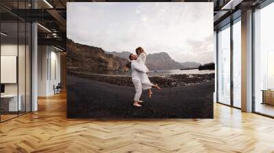 Male groom holding on hands female bride on the beach Wall mural