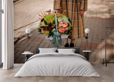 Woman in plaid coat holding a big wicker basket of beautiful autumn flower composition Wall mural