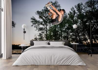 Young man dressed in casual clothing trampolining in a summer park Wall mural