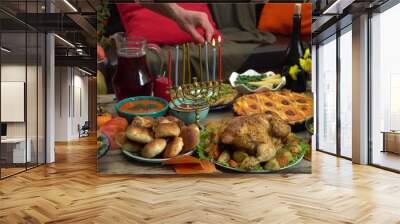 Lighting the Menorah lights. Menorah candles. Festive Hanukkah dinner at home with family. Traditional kosher Jewish food on the table - sufganiyot, latkes, cottage cheese and cheese meals Wall mural