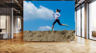 young woman running on mountain trail with blue sky background Wall mural