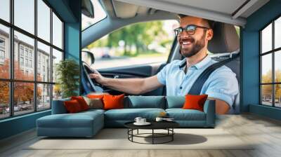 Handsome young man is driving a car and smiling. He is sitting on the steering wheel and looking at camera Wall mural