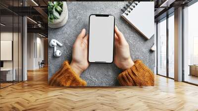 Mockup image of woman's hands holding smartphone with blank screen on gray table background, top view Wall mural