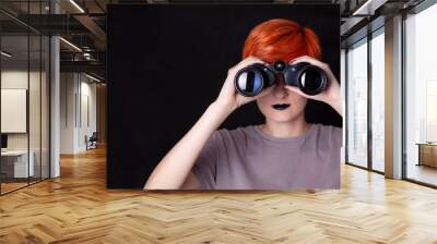 Young woman looking through binoculars isolated on black background Wall mural