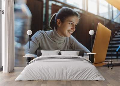 Happy smiling girl using laptop for studying in open work place Wall mural