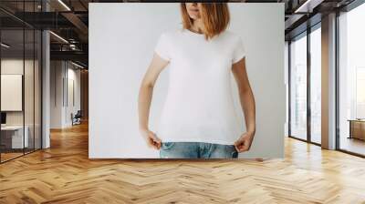 Young hipster girl wearing blue jeans and blank white t-shirt with area for your logo or design, mock-up of white t-shirt, white wall in the background Wall mural