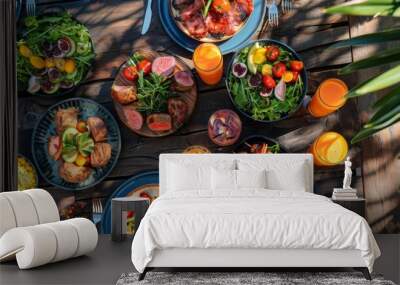 A top view of a stylish outdoor dining table set for a summer barbecue, with grilled meats, salads, and tropical cocktails laid out on colorful plates and glassware Wall mural