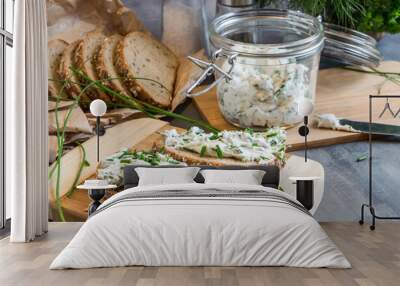 Home made bread on a wooden cutting board with curd cheese and ricotta and herbs. Decorated with green herbs  Wall mural