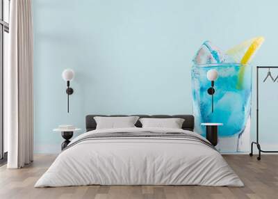 Alcohol juicy fruit blue cocktail with curacao liquor, lemon slice, ice cubes in frozen shot glass in modern elegant pastel blue interior. Wall mural