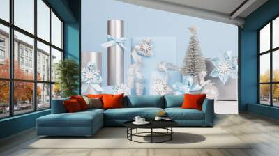 Elegance soft christmas home decorations - silver small fir with blue and metallic gift boxes with shiny ribbons and snowflakes on light white wood board and pastel blue wall. Wall mural