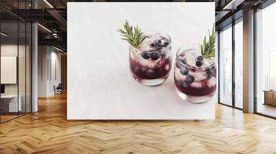 Fresh cold summer fruit cocktails with ice cubes, blueberry, rosemary on white wood board, top view. Wall mural