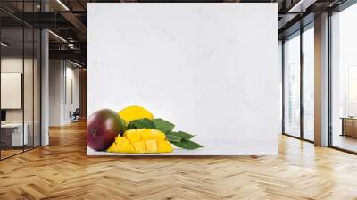 Juicy mango with ripe yellow sliced half and green leaves on soft light white wood background. Elegant moder kitchen interior with tropical fruit. Wall mural