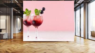 Red north homemade liquors in two wineglasses with ice cubes, blueberry, green mint on soft pastel pink background and white wood table, copy space. Wall mural