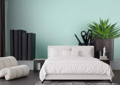 Simple minimalistic office interior with black stationery, books, coffee cup, aloe plant in pot in elegant green mint menthe interior on white wood table, copy space. Wall mural