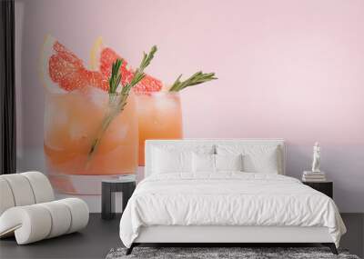 Summer cold cocktail with ice cubes, juice and slices grapefruit on pastel pink background. Wall mural