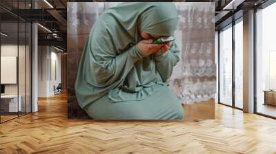 A Muslim woman in a light dress for prayer performs prayer while sitting on a mat Wall mural