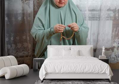 A Muslim woman in a light prayer dress kneeling on a mat reads prayer with her hands raised Wall mural