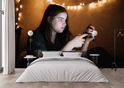 Young woman using smart phone sitting in bed at home at night Wall mural