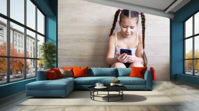 girl child with pigtails talking on the phone, getting homework on a cellular connection, during isolation and a pandemic, a convenient means of communication Wall mural