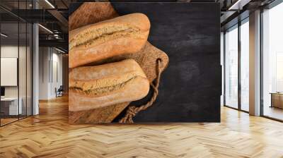 Two whole rustic bread rolls on wooden cutting board on dark table Wall mural