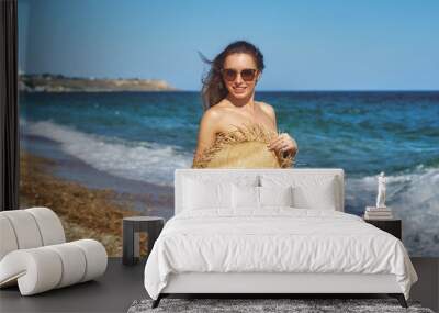 Happy young woman enjoying a beach holiday . A beautiful model in a bikini wears a wide-brimmed hat Wall mural