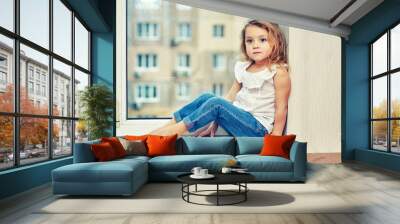 Portrait of a little girl sitting on a windowsill in the house Wall mural