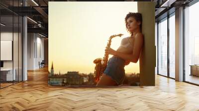 young girl with saxophone on the roof parapet. woman holding a musical wind instrument. young musician looking for inspiration Wall mural