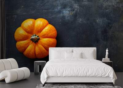 A dark charcoal surface featuring a single bright orange pumpkin, the texture and color standing out vividly Wall mural