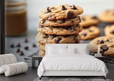 A stack of peanut butter and chocolate chip cookies, freshly baked and arranged on a cooling rack, with a jar of peanut butter and scattered chocolate chips nearby Wall mural