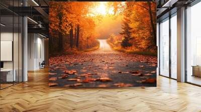 An autumn landscape featuring a long, winding road lined with trees in full fall color, with a thick carpet of leaves covering the road and the distant hills bathed in the golden light of sunset Wall mural