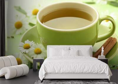 Cup of green tea with chamomile, isolated on a soft green background with decorative chamomile flowers and cinnamon sticks Wall mural